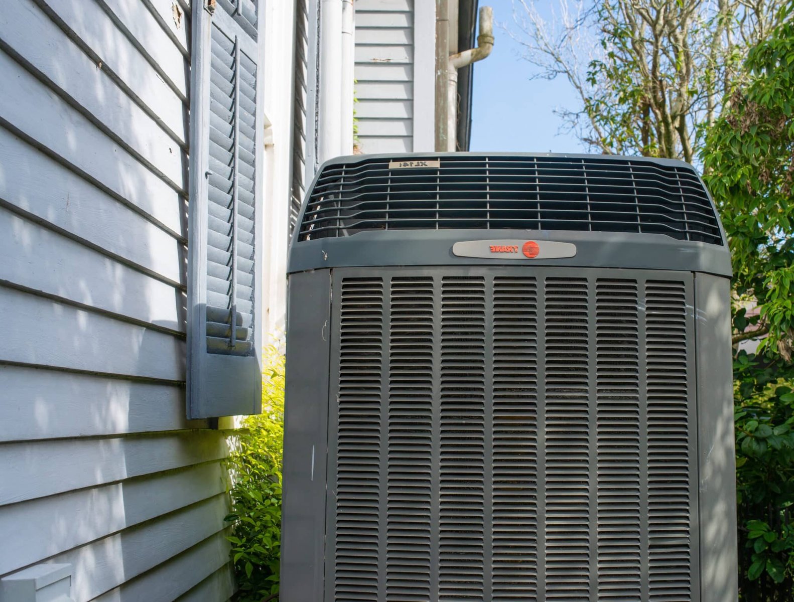 Trane residential air conditioning condenser unit installed beside a Katy, TX home with white shutters