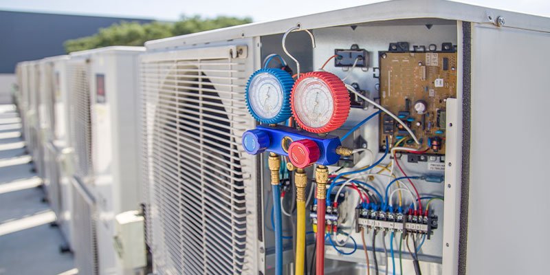HVAC technician servicing rooftop air conditioning units with refrigerant gauges and electrical panel access